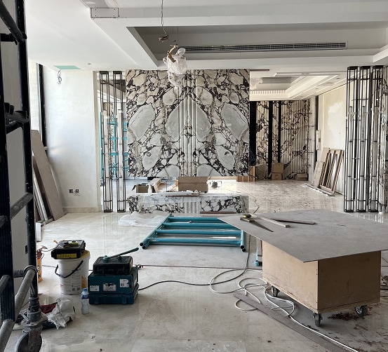 Chantier de luxe : pose de panneaux de marbre veiné et finitions intérieures en cours, ouvrier travaillant au plafond.