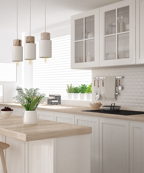 Cuisine moderne bois et blanc : style scandinave épuré Cuisine moderne et lumineuse avec îlot central, comptoirs en bois clair, armoires blanches à portes vitrées, et trois suspensions bois-blanc au-dessus du plan de travail.